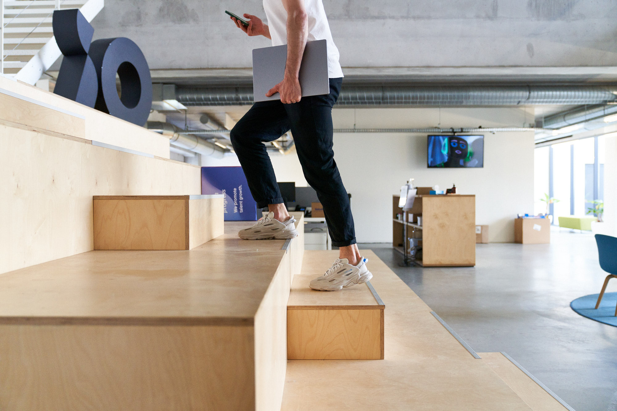 En person går uppför en trappa med en mobil i ena handen och en dator under andra armen